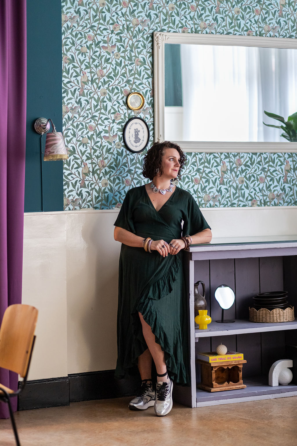 Elianne Alblas in een groene jurk, leunend tegen een toonbank in een sfeervol horeca-interieur